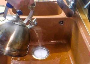 Boiling water from a kettle is poured into the sink drain