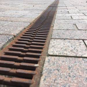 Surface linear drainage system with cast iron gratings, mounted in paving stones.