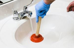 A gloved hand holds a plunger in a sink